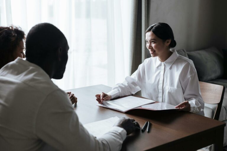 A diverse group discussing documents with a professional in a home interior setting.